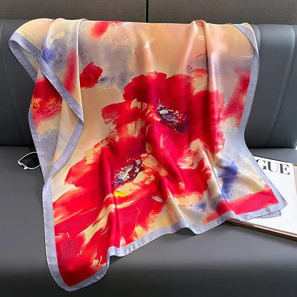 Silk scarf with bold red floral print and soft purple border on a gray sofa