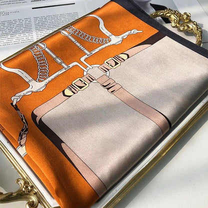 Silk scarf with orange, tan and horse bridle print on a tray and an open magazine