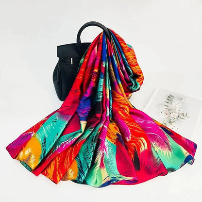 Colorful silk scarf with feather print draped over a black handbag on white background