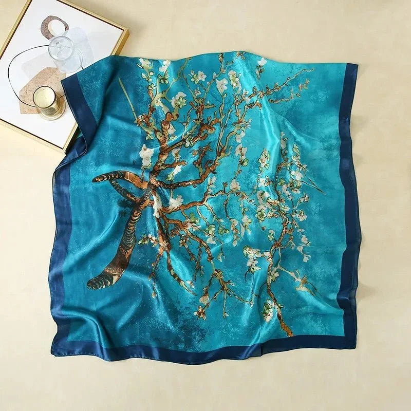 Blue silk scarf with an almond blossom branch print on a flat beige surface