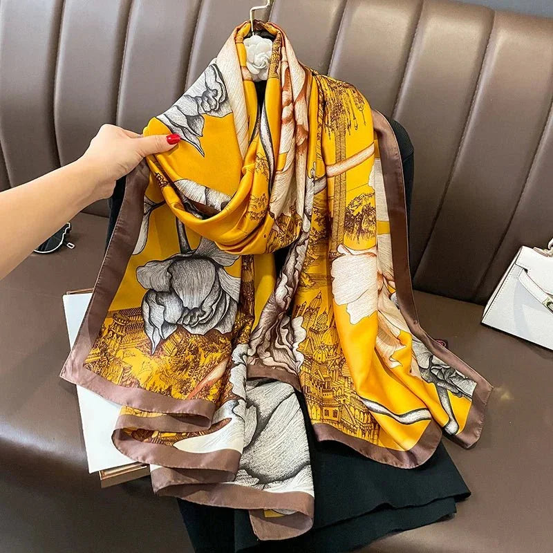 Yellow silk scarf with floral and cityscape print, brown border, displayed on a bench