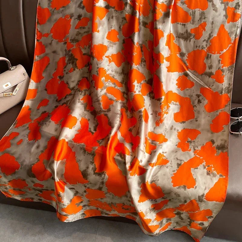 Silk scarf with orange and gray abstract pattern draped on a sofa