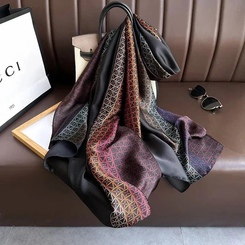 Silk scarf with geometric pattern draped on a beige handbag, sunglasses and shopping bag nearby