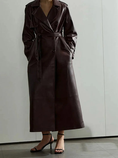 Long dark brown faux leather trench coat with belt worn by a model in black strappy heels