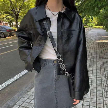 Woman wearing a black faux leather shirt jacket with a white top and gray skirt standing on a tree-lined street