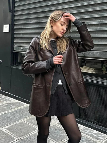 Woman wearing a dark brown leather jacket and black skirt posing against a metal shutter in urban setting